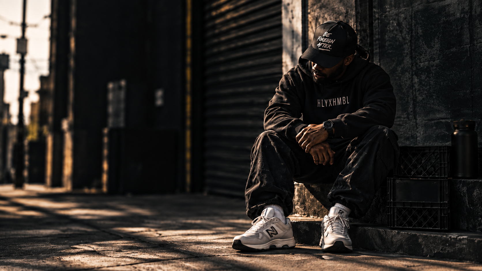 Model wearing HLYXHMBL apparel seated in an urban setting