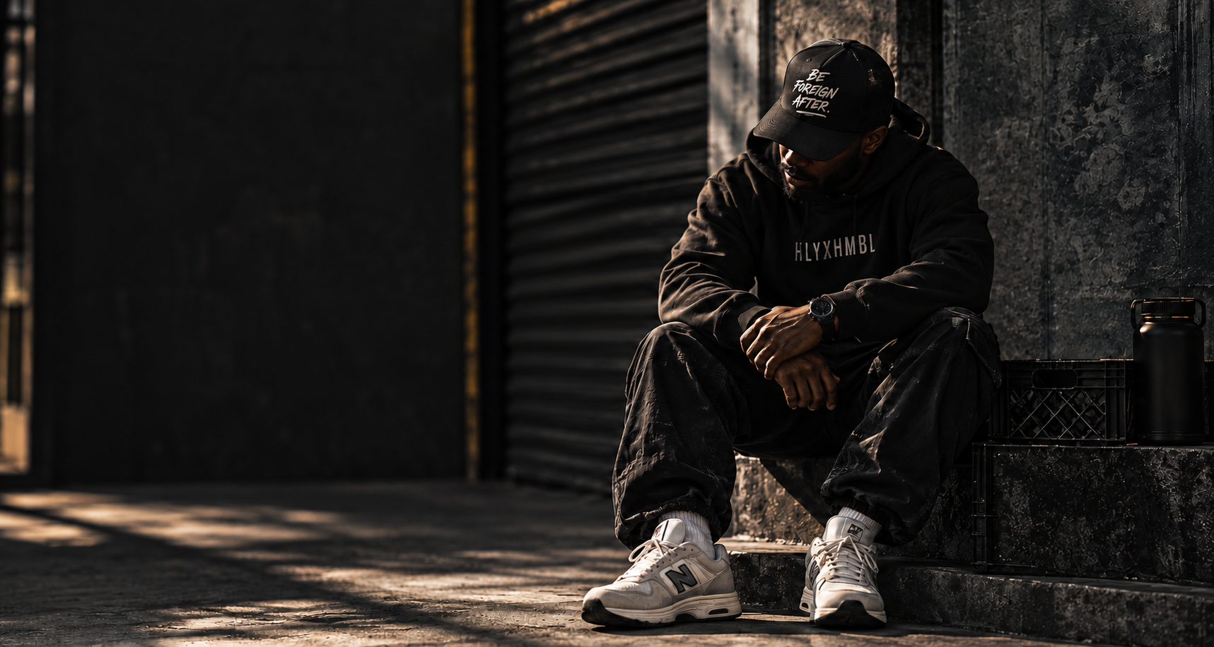 Model in HLYXHMBL apparel seated beside a dark wall